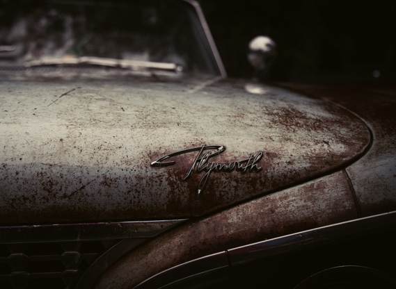 Rusted vintage Plymouth hood covered in dust